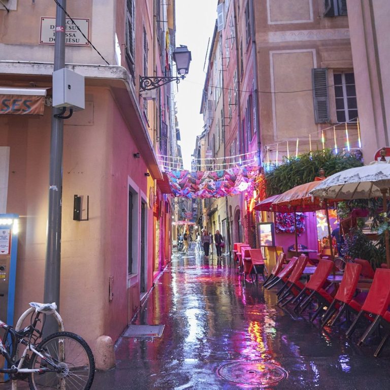 Ruelle étroite et colorée, décorée de lumières, après la pluie, avec des tables extérieures.