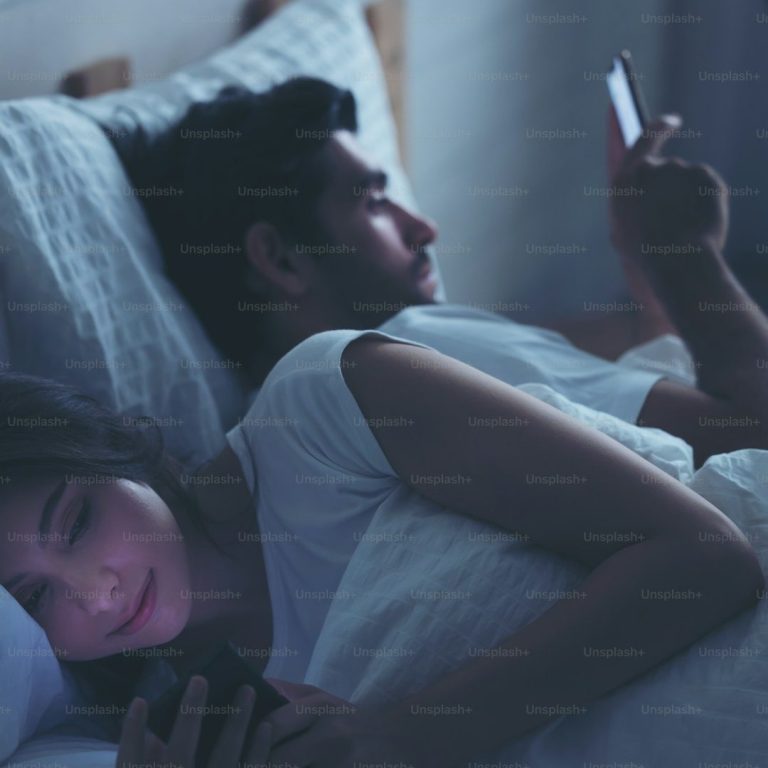 affaire famille Un couple dans un lit, chacun sur son téléphone, avec des expressions concentrées.