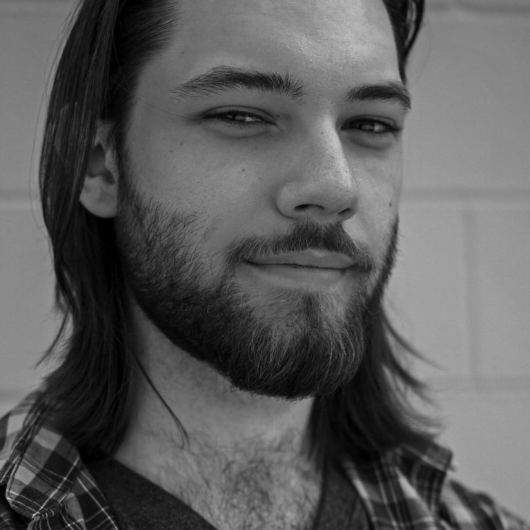 Portrait en noir et blanc d'un homme avec une barbe et des cheveux longs, souriant légèrement.