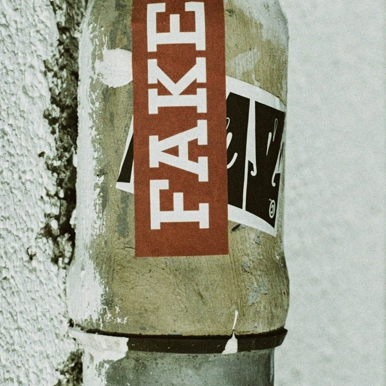 Bouteille avec une étiquette "FAKE" collée sur un mur texturé.