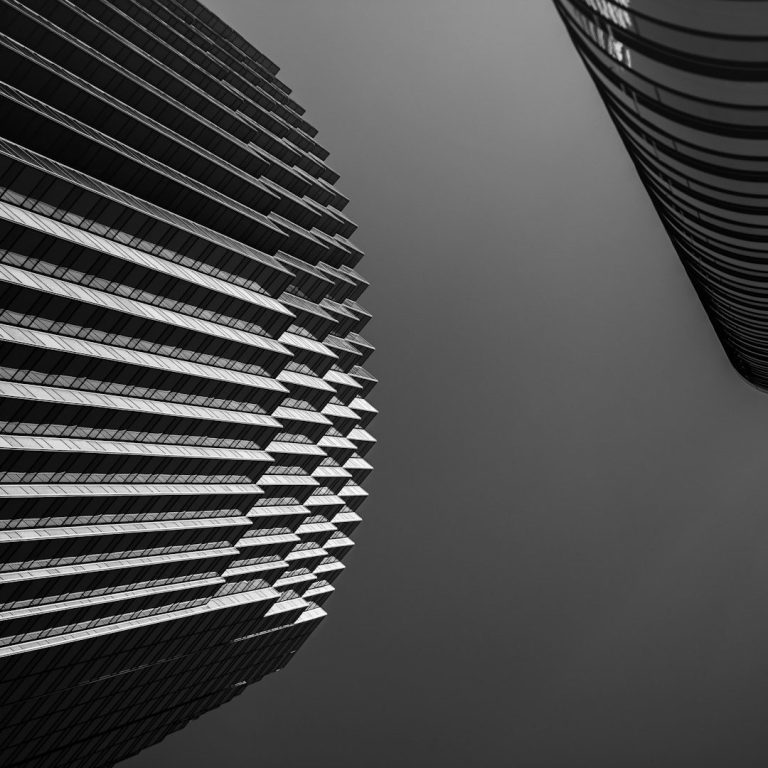 Vue en contre-plongée de deux gratte-ciel en noir et blanc, avec des lignes géométriques.