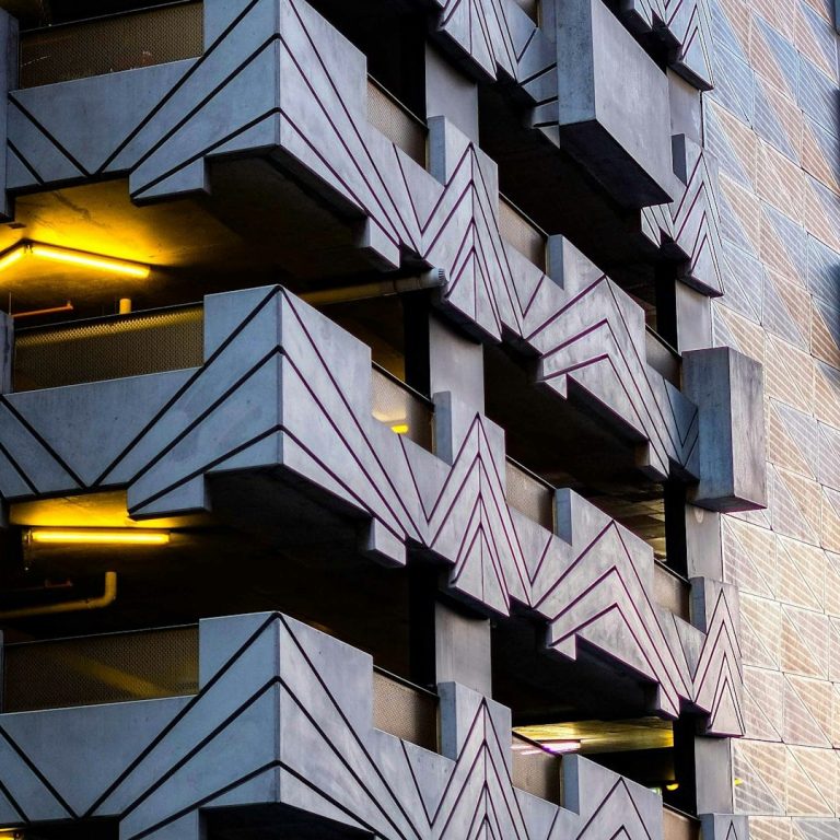 Bâtiment moderne en béton avec motifs géométriques et éclairage jaune.