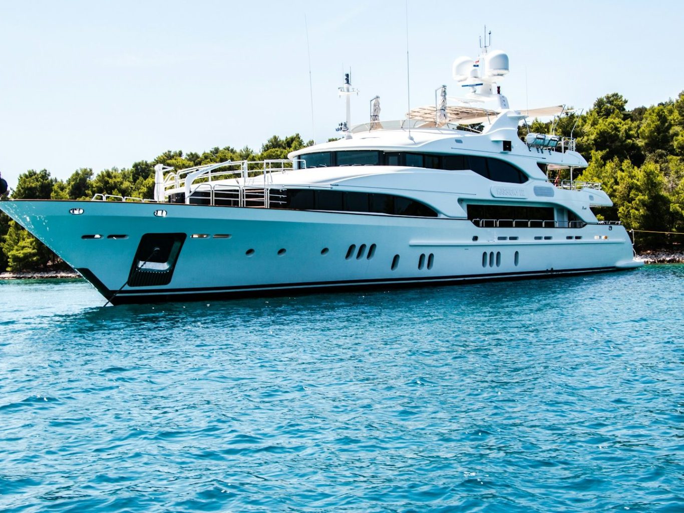 Yacht blanc de luxe amarré dans une eau turquoise, entouré de verdure.