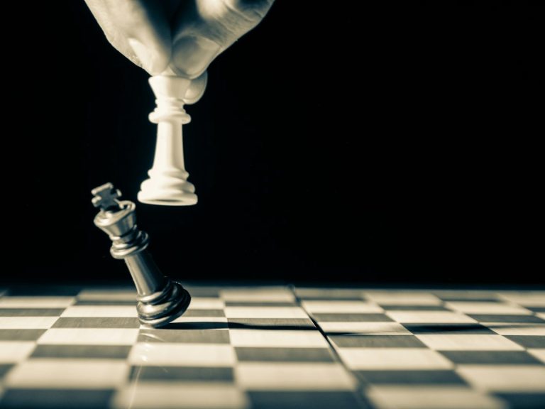 Une main déplace un roi blanc sur un damier, tandis qu'un roi noir est renversé.