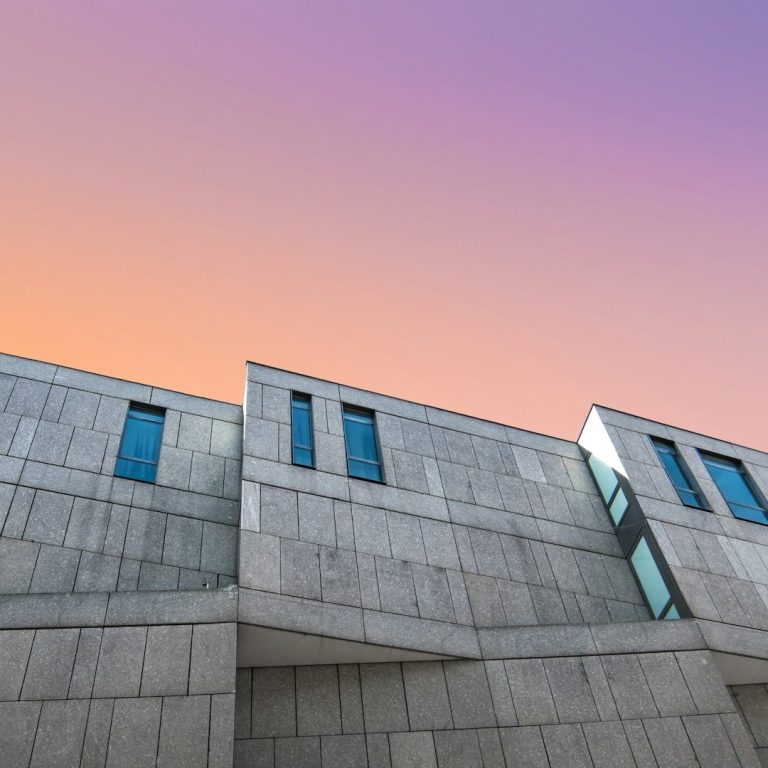 Façade moderne en béton avec fenêtres, sous un ciel dégradé pastel.