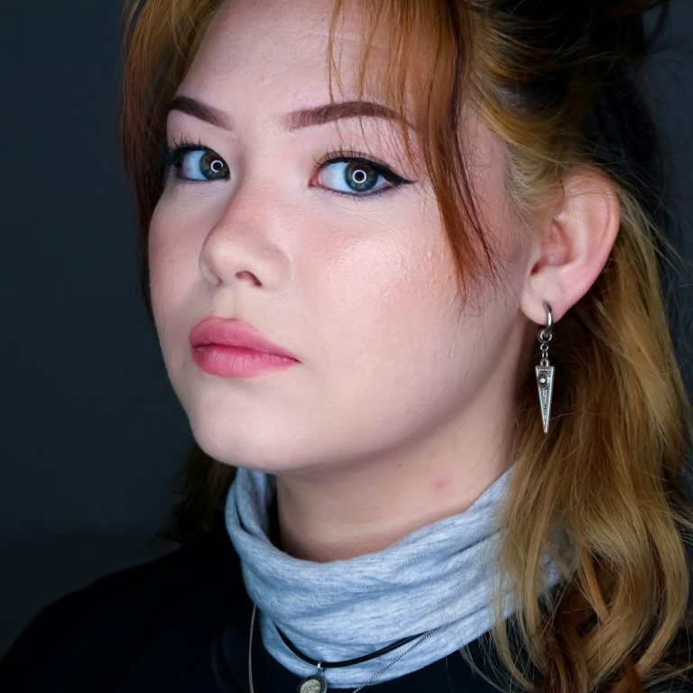 Femme au regard pénétrant, cheveux blonds, portant des boucles d'oreilles et un col.