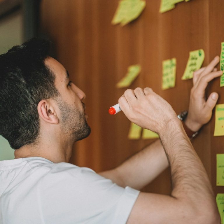 Homme utilisant un marqueur pour écrire sur des post-its collés au mur.