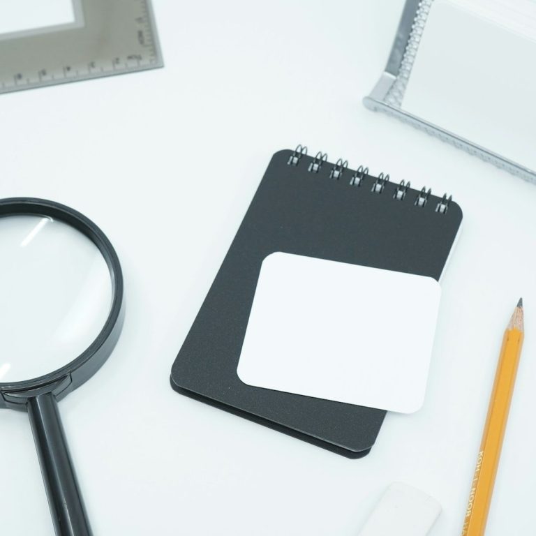 Bloc-notes noir, loupe, crayon et espaces vides pour notes sur fond blanc.